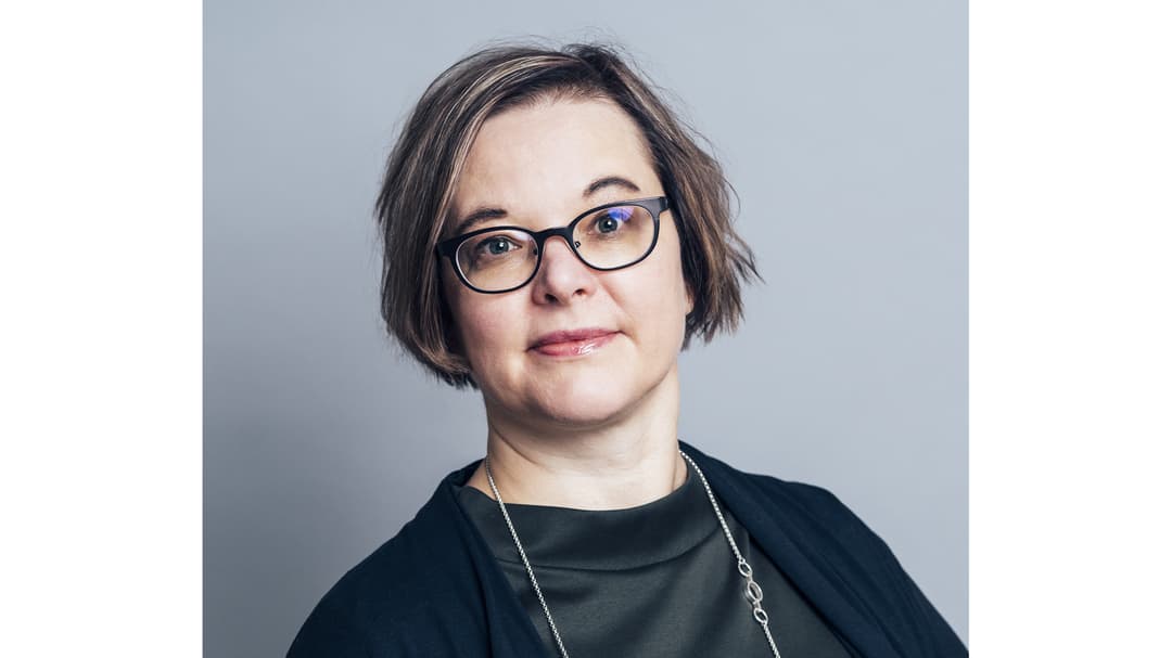 A woman with dark hair, glasses, wearing a black top.