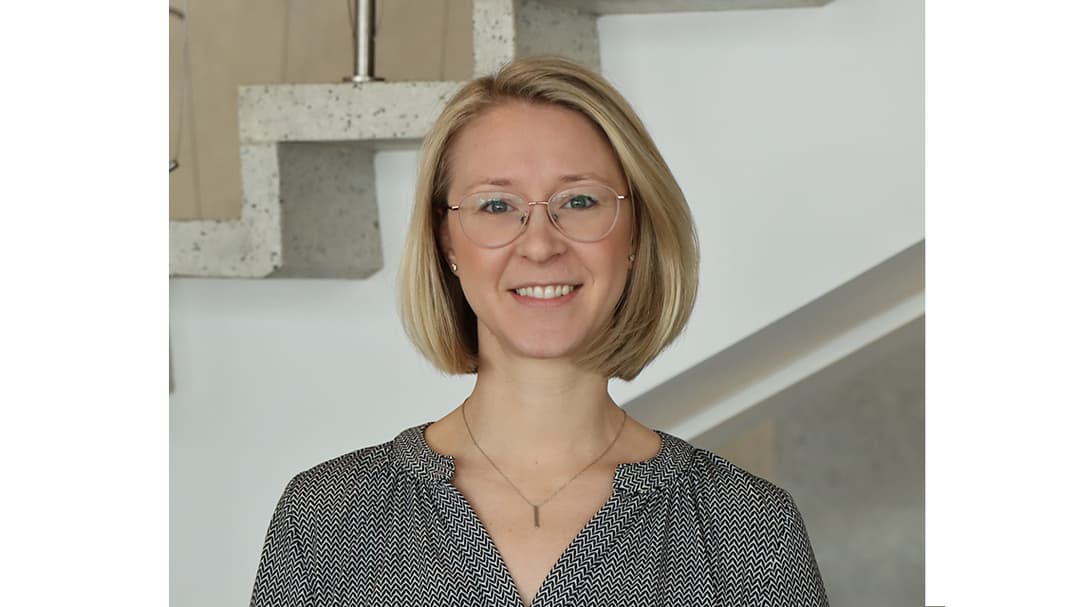 A fair-haired woman with glasses and a gray blouse.