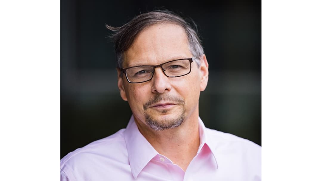 A dark-haired man in glasses, wearing a pink shirt.