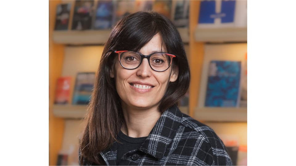 A woman with dark long hair, glasses and wearing a plaid shirt.