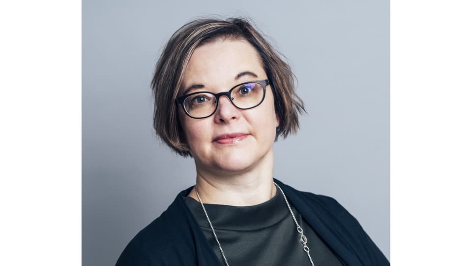 A woman with dark hair, glasses, wearing a black top.