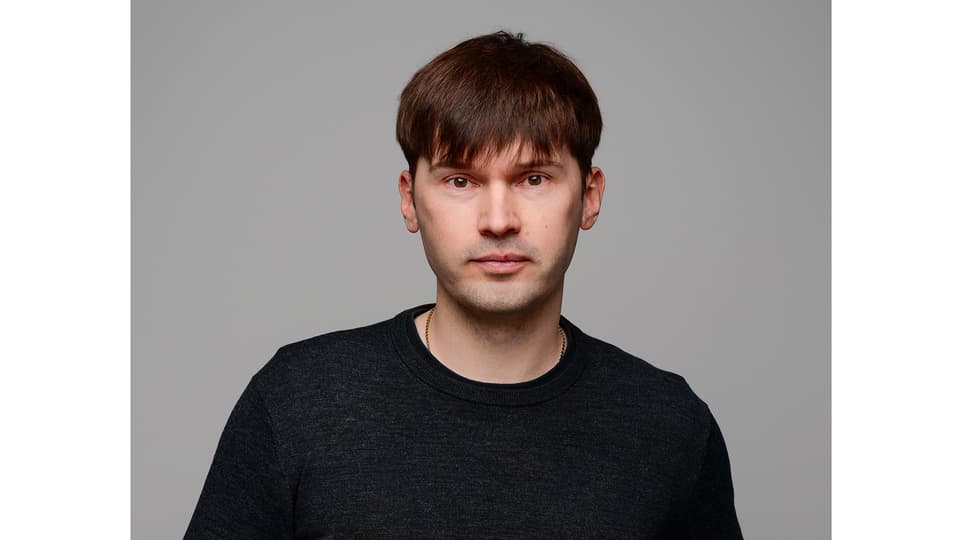 A man with dark, short hair, wearing a black shirt.